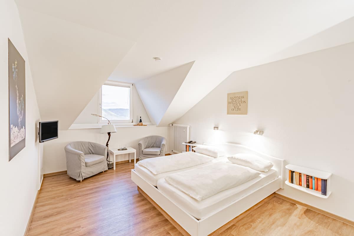 Un dormitorio moderno con techo estilo loft, una cama, dos sillas, una mesita y una estantería.