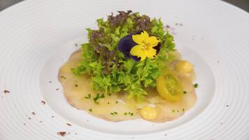 Ein weißer Teller mit Salat, einer gelben Blume und ein paar grünen Blättern.