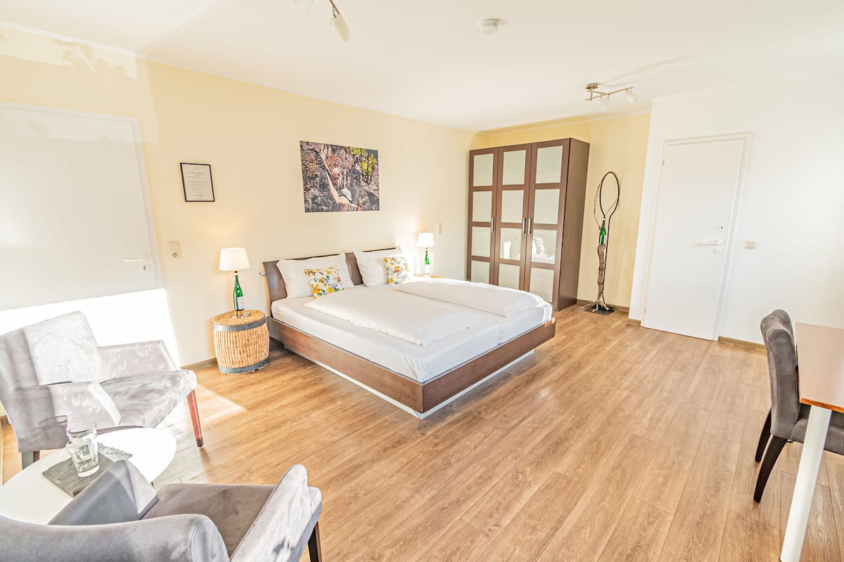 Una habitación de hotel moderna con una cama grande, una zona de estar con una silla y una mesa, y un armario.