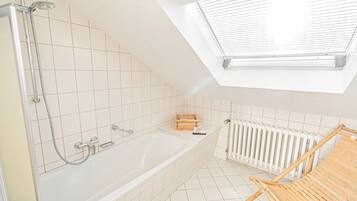 A modern bathroom with a skylight, a bathtub, a shower, and a wooden bath mat.