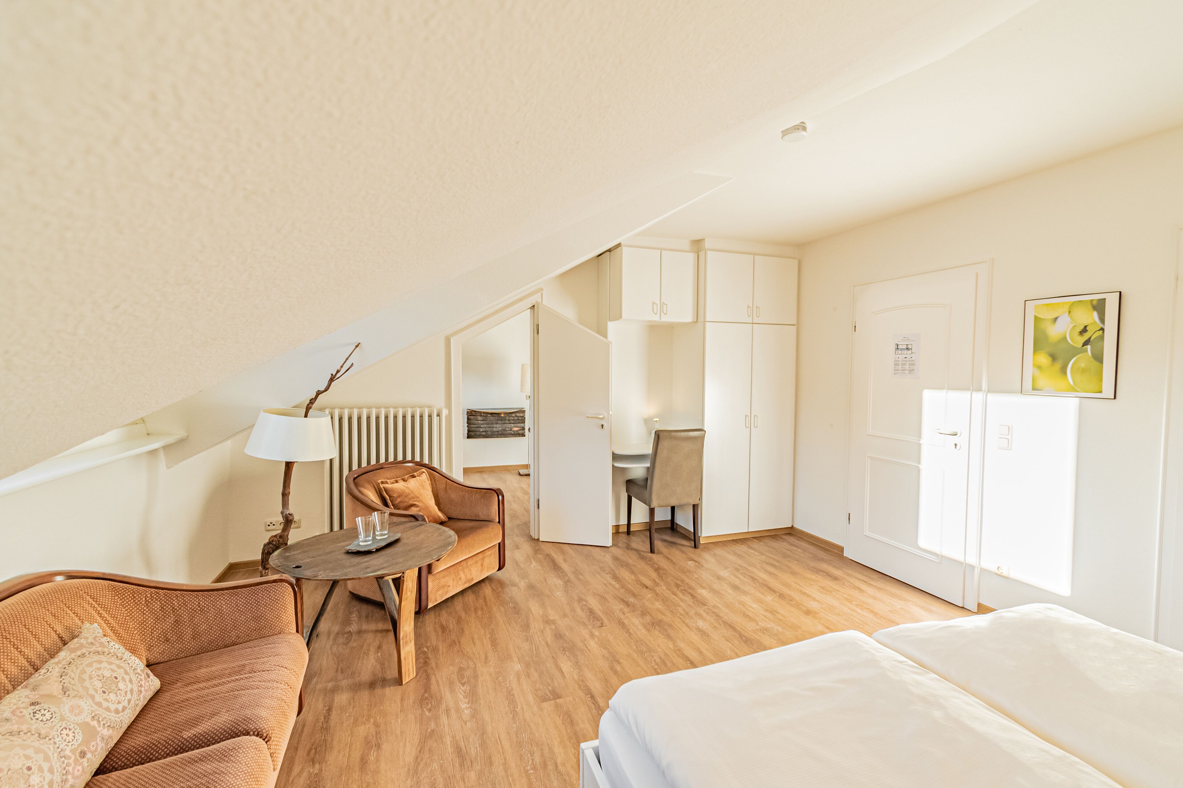 Una camera d'hotel con pavimento in legno, un letto, un divano, una scrivania e una sedia.