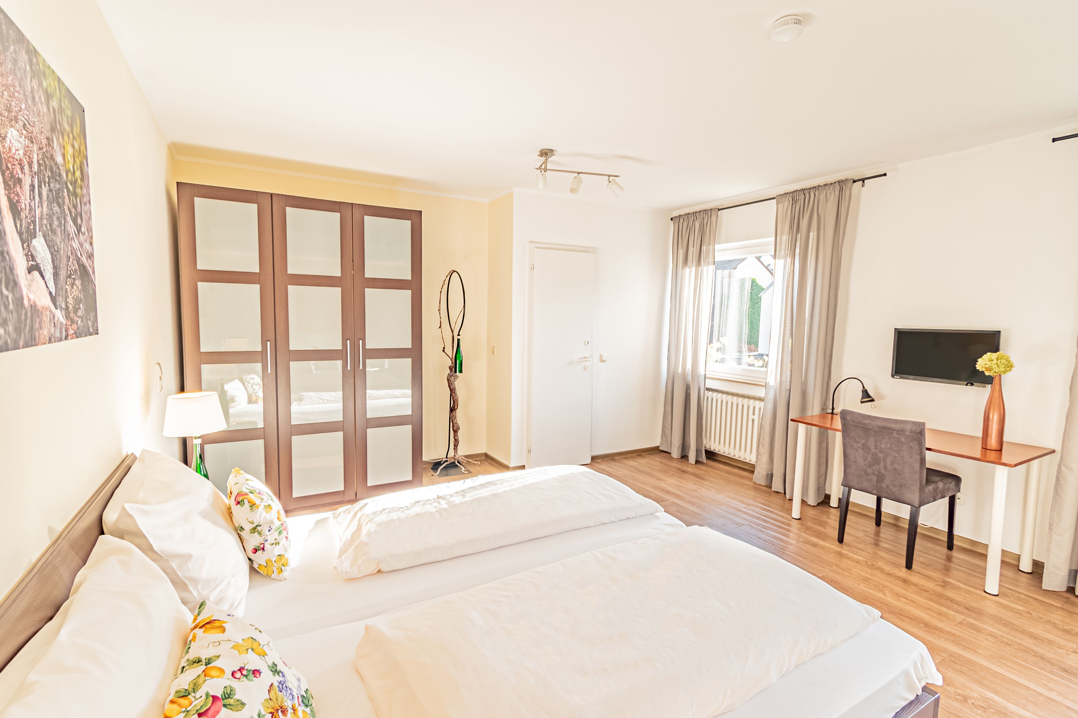 Habitación de hotel con dos camas, un escritorio, una silla, un televisor y un ventanal con cortinas.