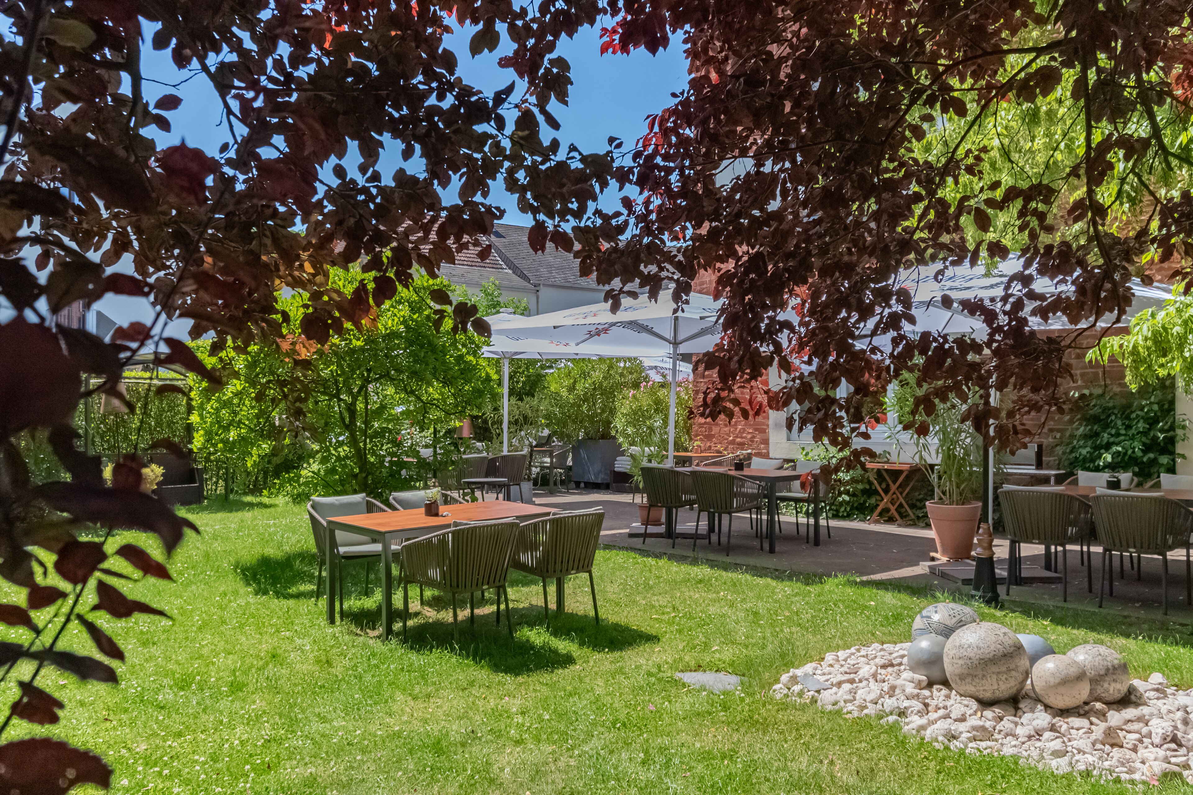An outdoor patio area with tables and chairs, surrounded by greenery and a brick wall.