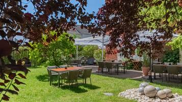 An outdoor patio area with tables and chairs, surrounded by greenery and a brick wall.