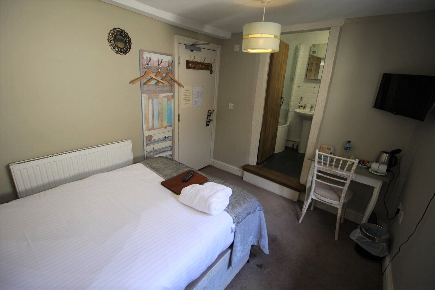 Una habitación de hotel con una cama, un escritorio con una silla, un espejo y una televisión.