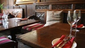 Un restaurante con mesas y bancos de madera, cristalería transparente y servilletas ordenadas.