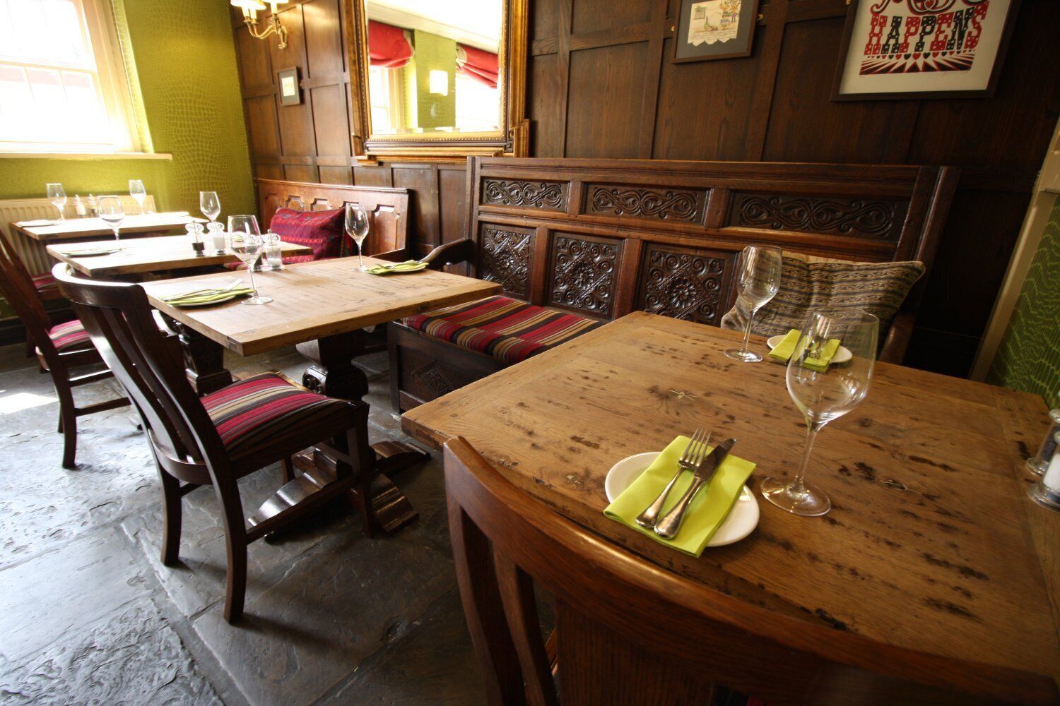 A restaurant interior with wooden tables and benches, some with wine glasses and cutlery.