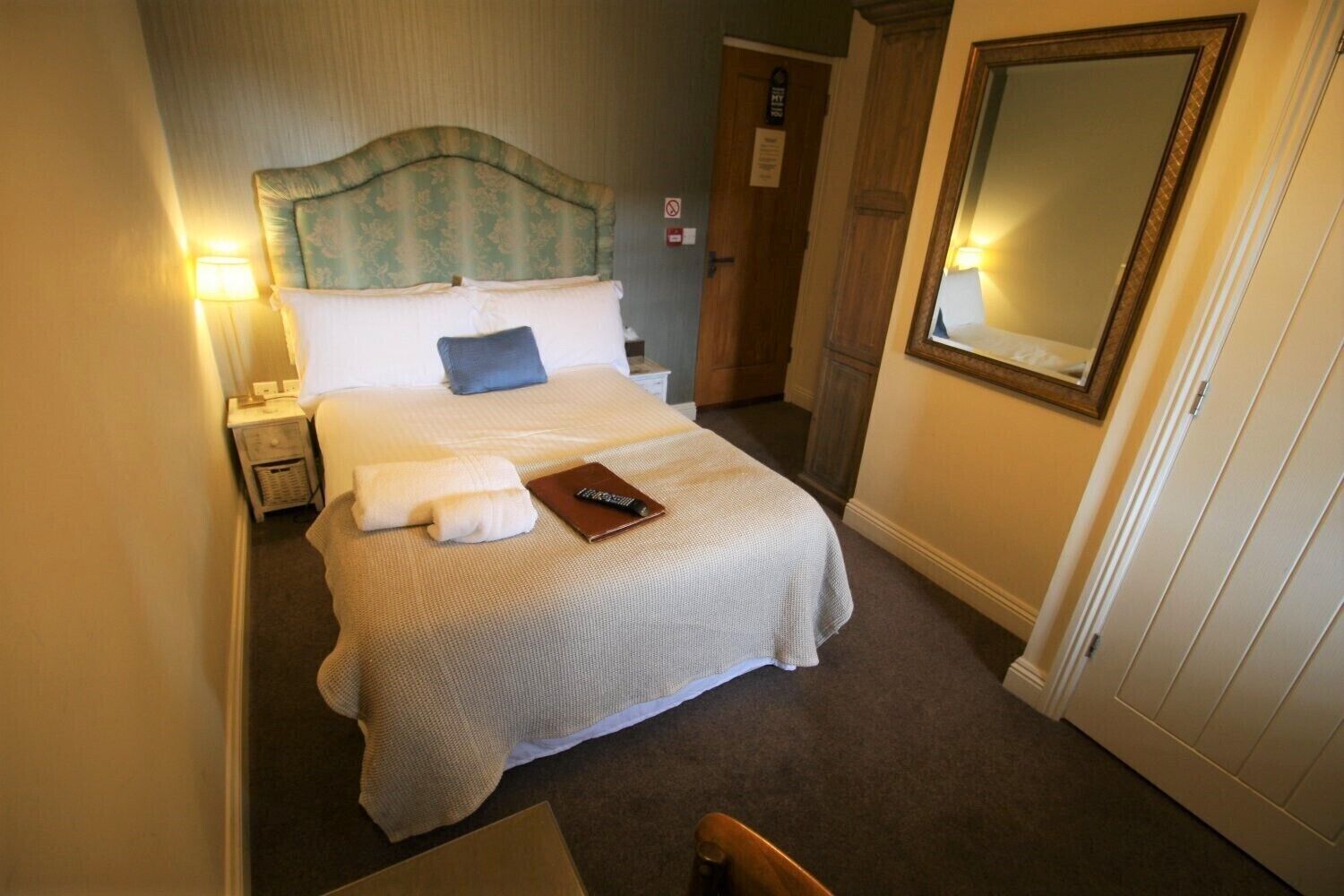 Una habitación de hotel con una cama, una mesita de noche, un control remoto y un espejo.