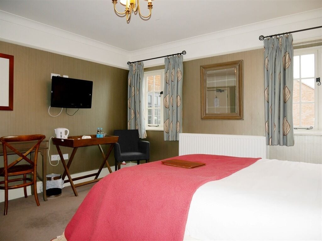A hotel room with a bed, a desk, a chair, a television, and curtains.