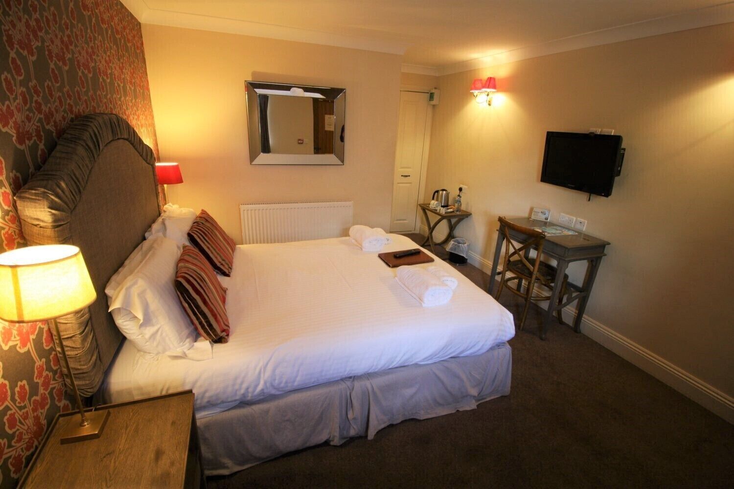 A hotel room with a large bed, a desk, a television, and a mirror.