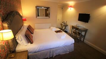 A hotel room with a large bed, a desk, a television, and a mirror.