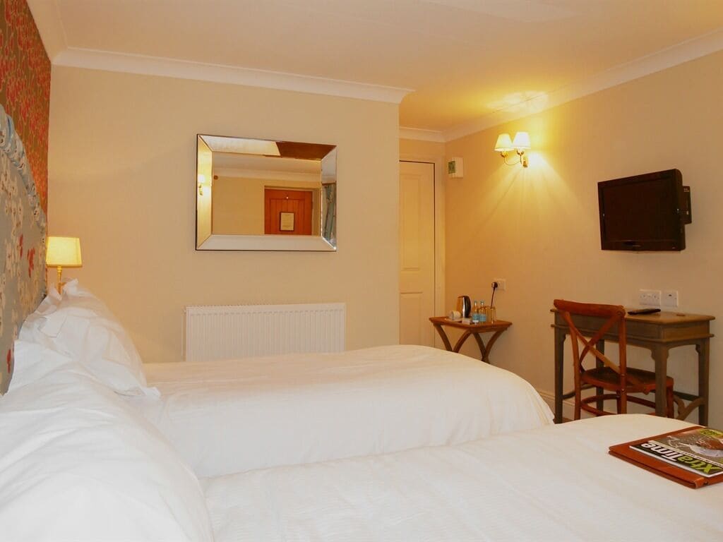 A hotel room with two beds, a desk with a chair, a television, and a mirror.
