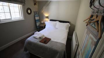A neatly made bed with white linens and a remote control on a wooden tray.