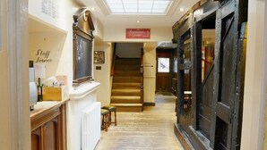 Un pasillo estrecho con piso de madera, una escalera que sube a un nivel superior y un letrero que indica un restaurante y un jardín.