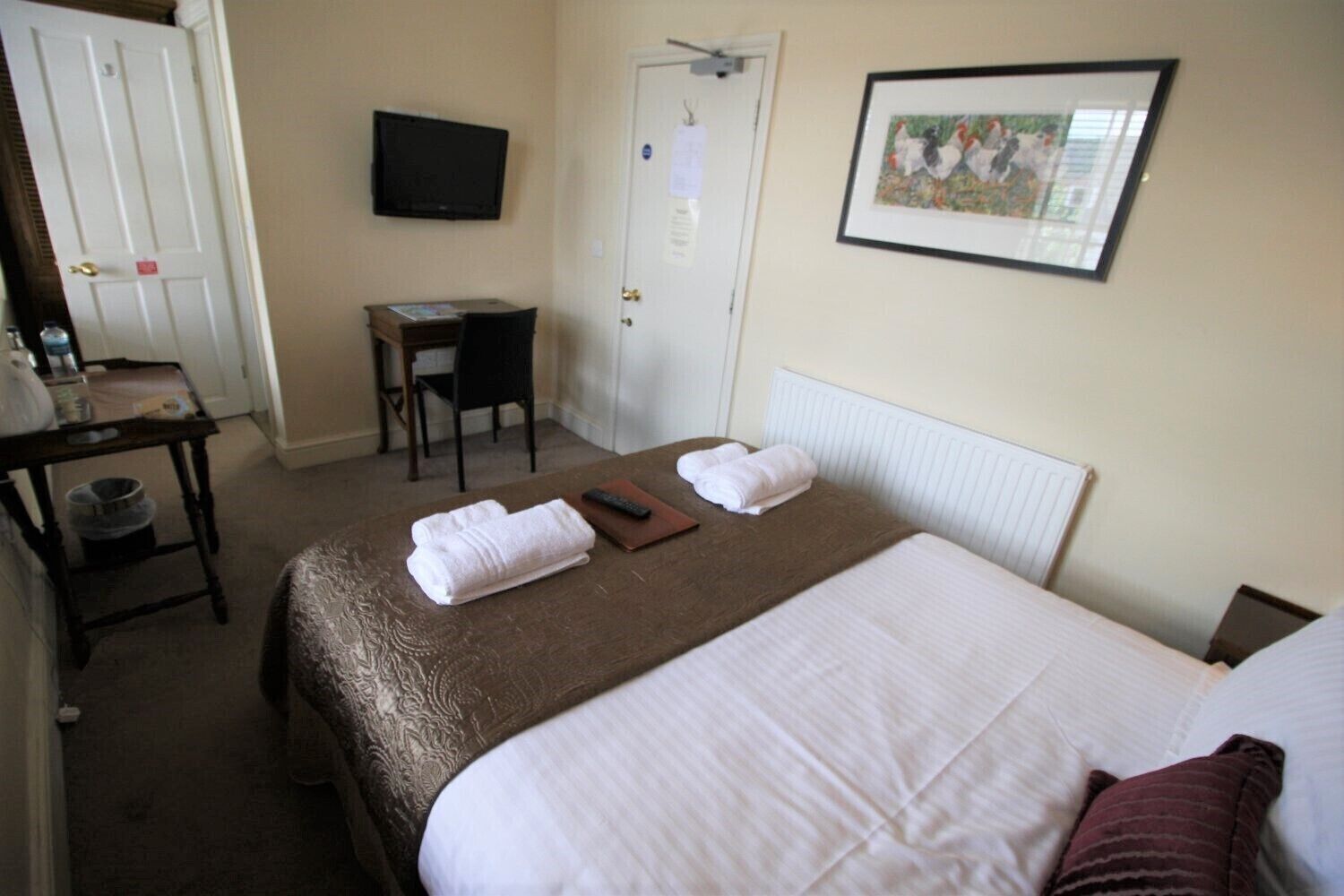 Ein Hotelzimmer mit einem Bett, einem Schreibtisch, einem Sessel, einem Fernseher und einem gerahmten Bild an der Wand.