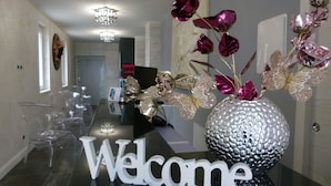 Een receptie met een 'Welcome' bord, een glazen vaas met decoratieve bloemen en een kroonluchter.