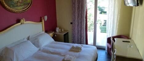 Ein Hotelzimmer mit Bett, Schreibtisch, Stuhl, Fernseher und einem Balkon mit Vorhängen.
