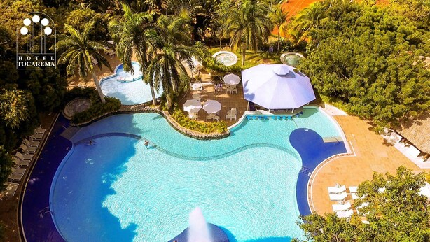 A large, multi-level swimming pool with a fountain, surrounded by palm trees and lounge areas. - Hotel Tocarema (Girardot)