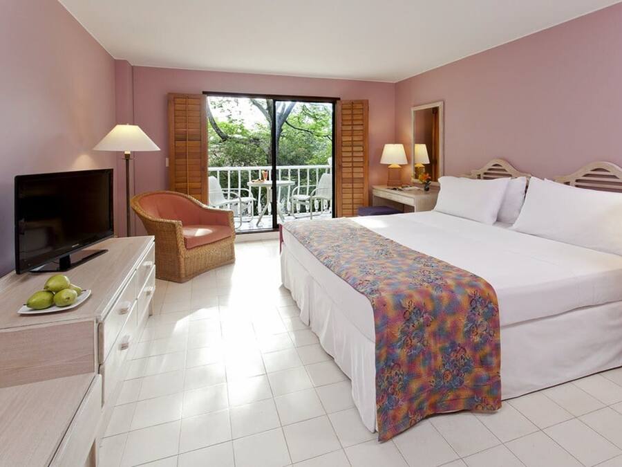 A hotel room with a bed, a television, a chair, a desk, and a balcony with outdoor furniture.