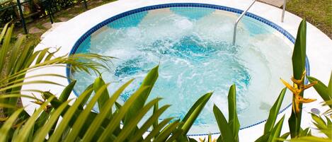 A circular hot tub surrounded by lush greenery and a metal railing.