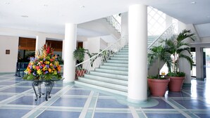 A spacious lobby with a central staircase, a decorative floral arrangement, and potted plants. - Hotel Tocarema (Girardot)