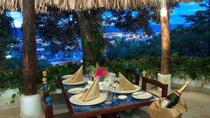 A table set for a meal with a bottle of champagne, surrounded by tropical plants and a view of a cityscape at dusk. - Hotel Tocarema (Girardot)