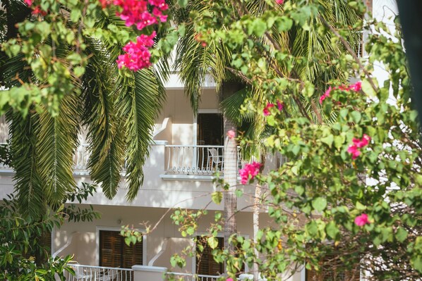 Un edificio de varios pisos con balcones, rodeado de exuberante vegetación y flores rosadas.