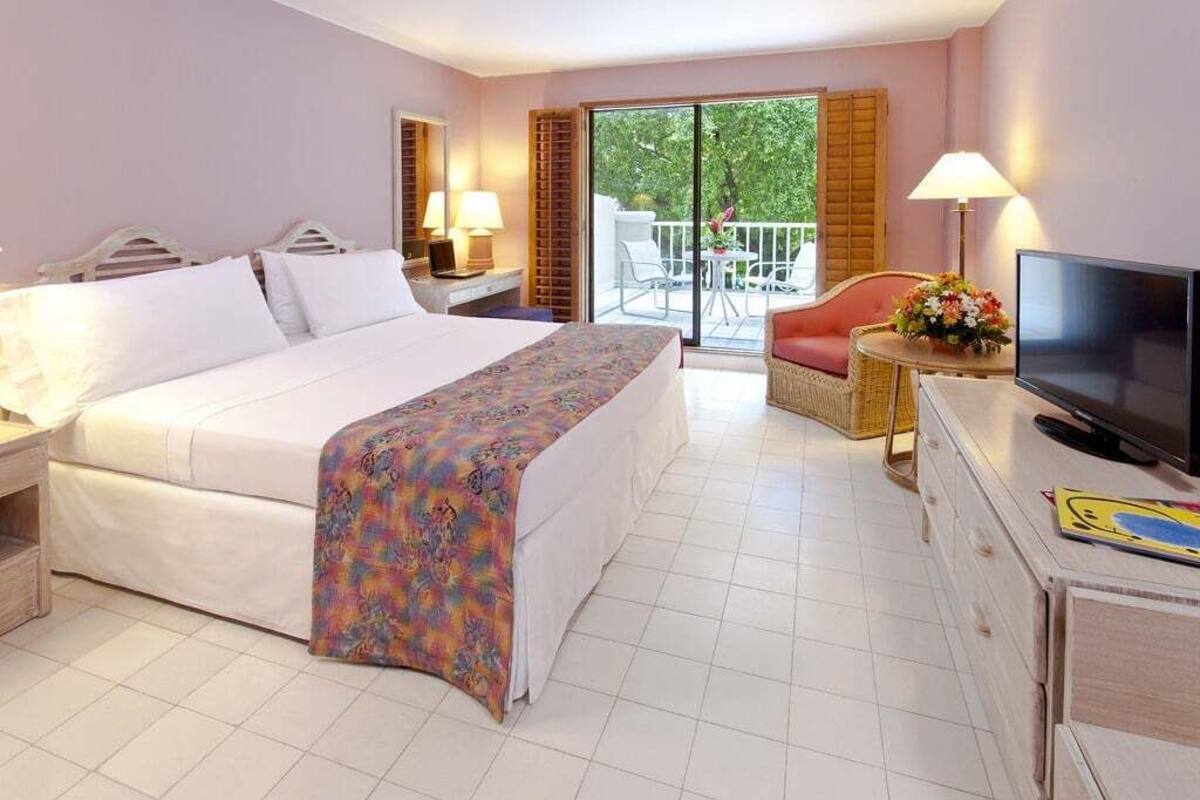 A hotel room with a bed, a television, a desk, a chair, and a balcony with a view of greenery.