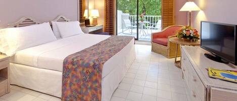 A hotel room with a bed, a television, a desk, a chair, and a balcony with a view of greenery.