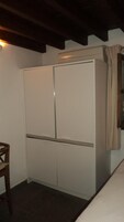 Una habitación pequeña con un armario blanco, una silla de madera y una ventana con cortinas.