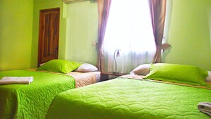Une chambre avec deux lits, chacun agrémenté de draps et d’oreillers verts, une porte en bois et une fenêtre avec des rideaux.