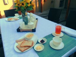 Una mesa de desayuno con pan, mantequilla, mermelada y un vaso de jugo.