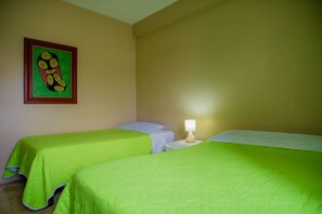 Una habitación con dos camas, una mesita de noche, una lámpara y un cuadro en la pared.