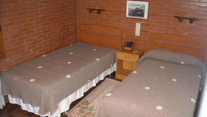 Une petite pièce avec deux lits simples, une table de chevet en bois, une petite table et un mur en briques.