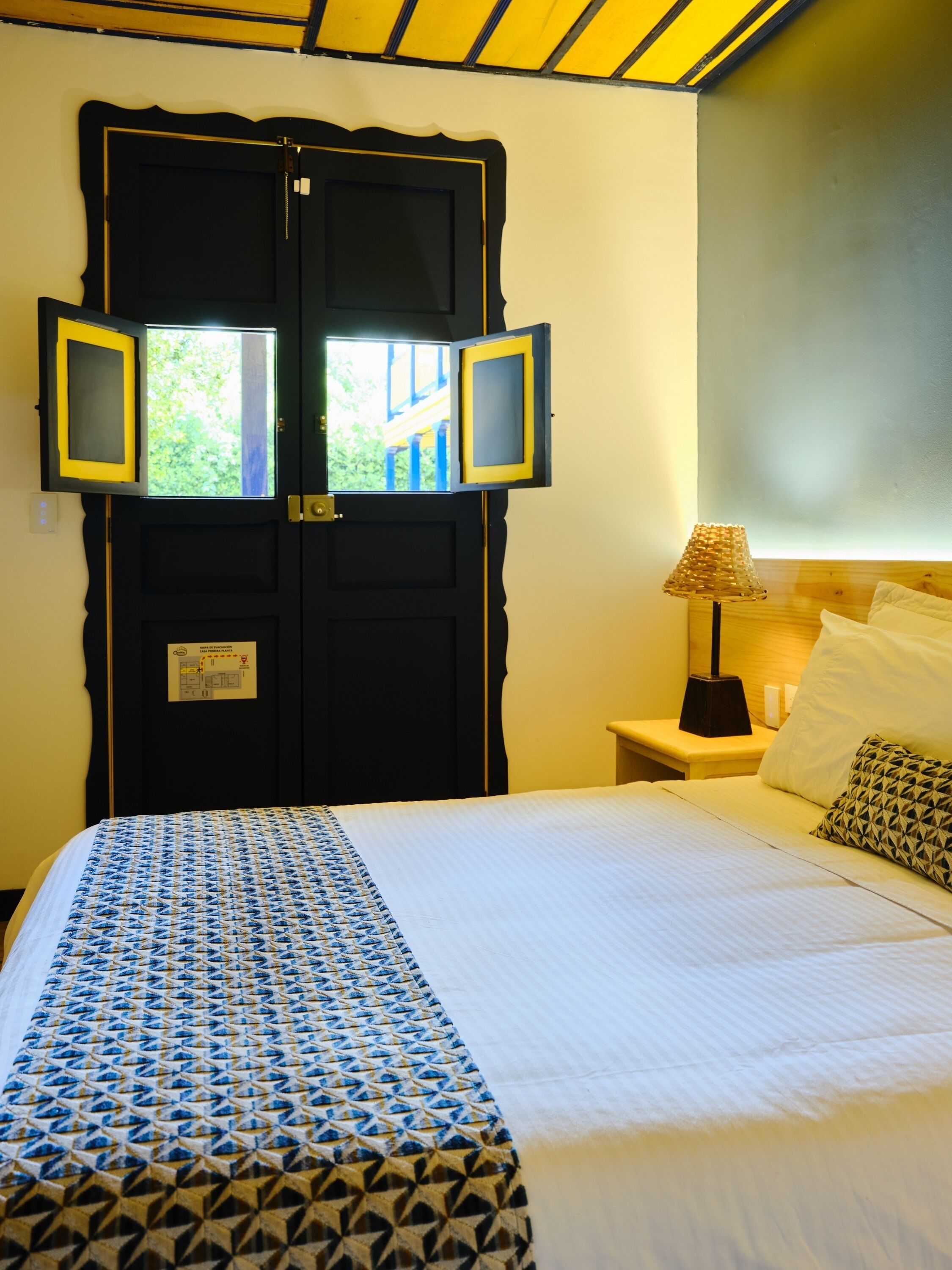 A hotel room with a bed, a nightstand with a lamp, and a door with two framed pictures.