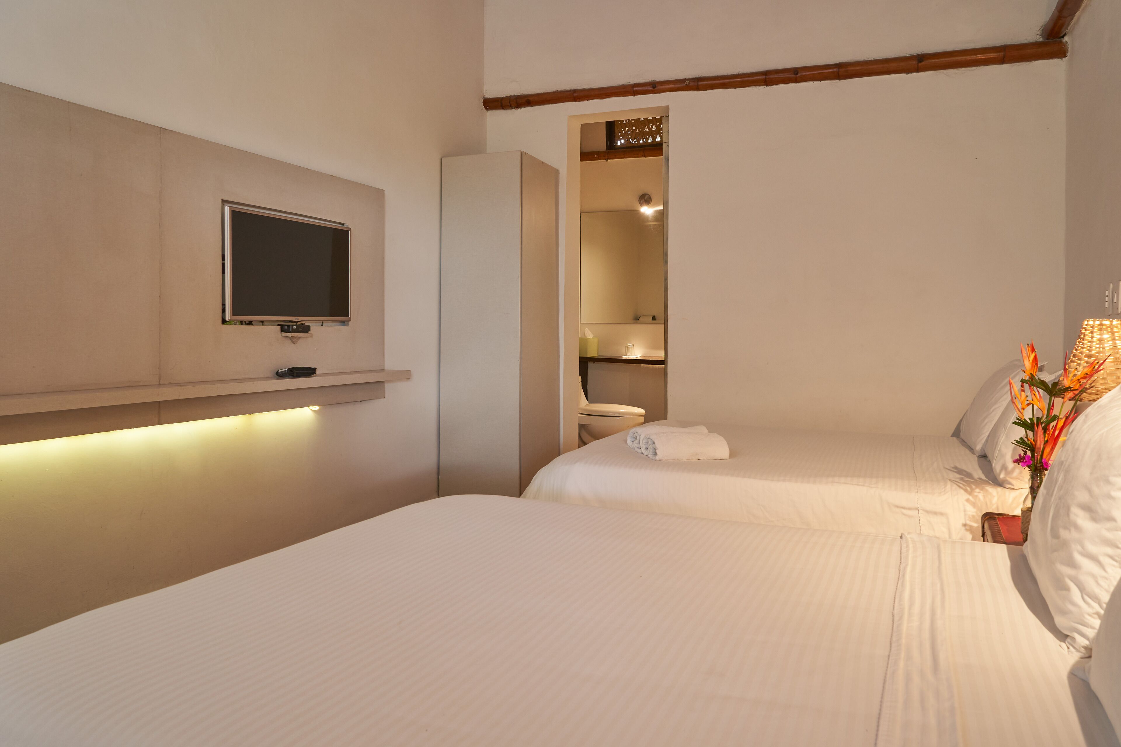 A hotel room with two beds, a television mounted on the wall, and a bathroom visible through an open door.