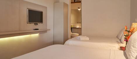 A hotel room with two beds, a television mounted on the wall, and a bathroom visible through an open door.