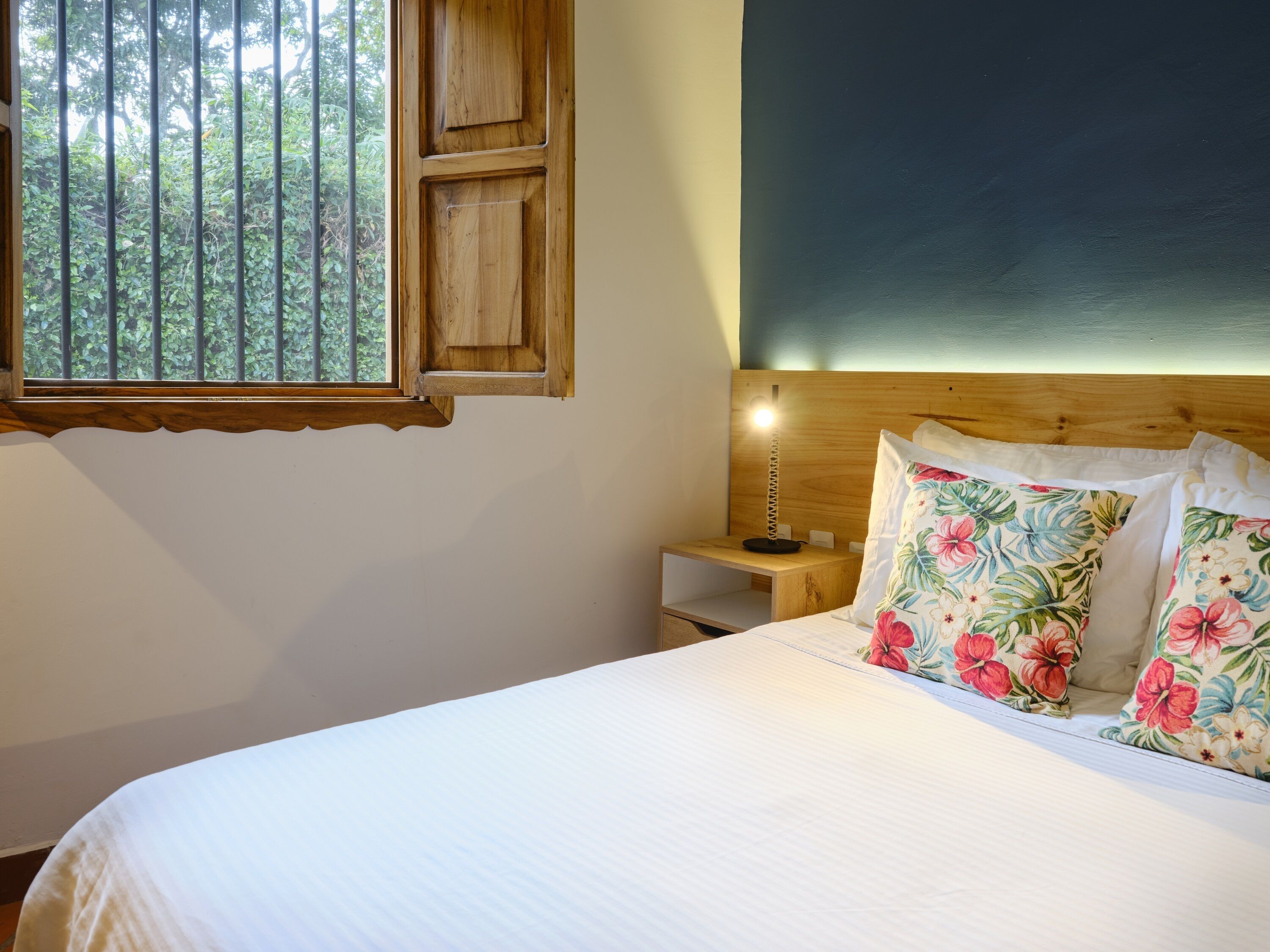 A bedroom with a wooden headboard, a bedside table with a lamp, and floral pillows.