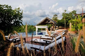A pool area with lounge chairs and a thatched-roof structure.