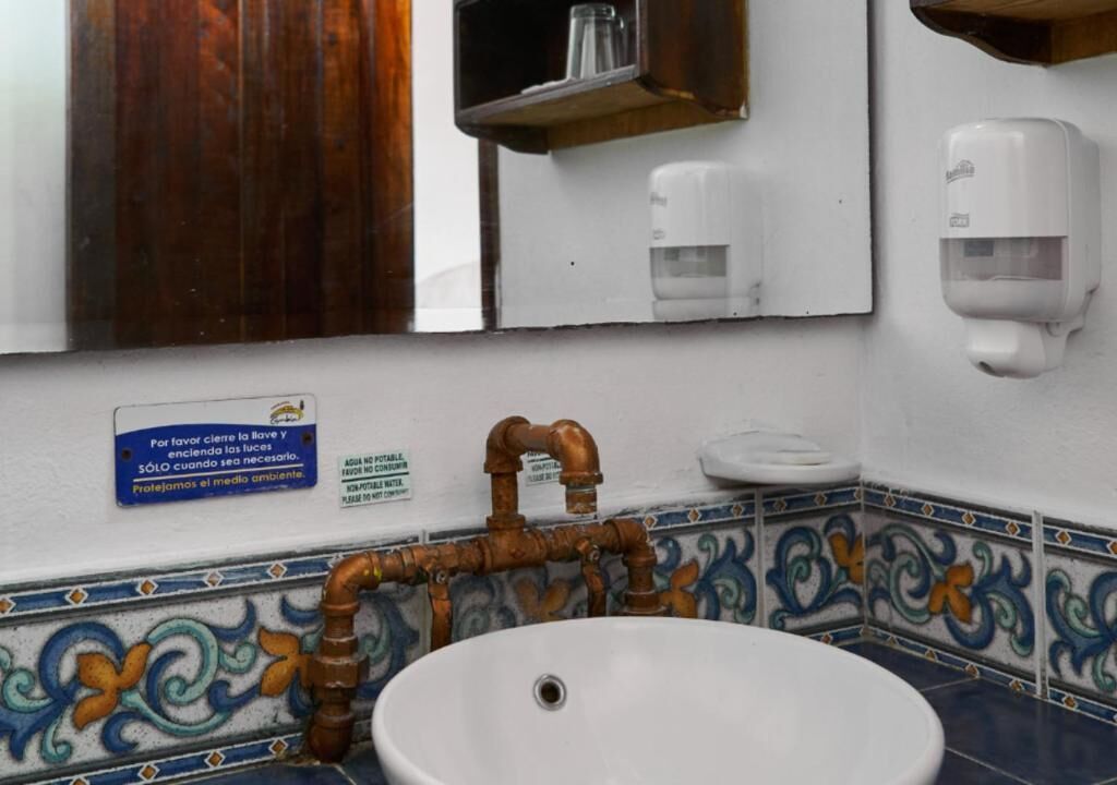 A bathroom with a white sink, a mirror, a soap dispenser, and a sign in Spanish.