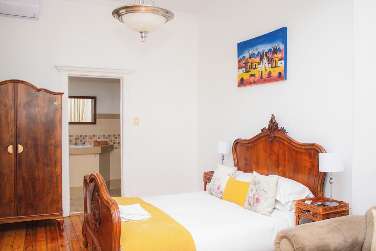 A bedroom with a wooden bed, a nightstand, a lamp, a painting, and a wardrobe.