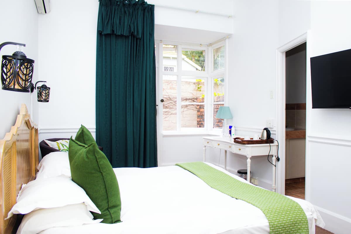 A bedroom with a bed, a desk, a window, and a television.