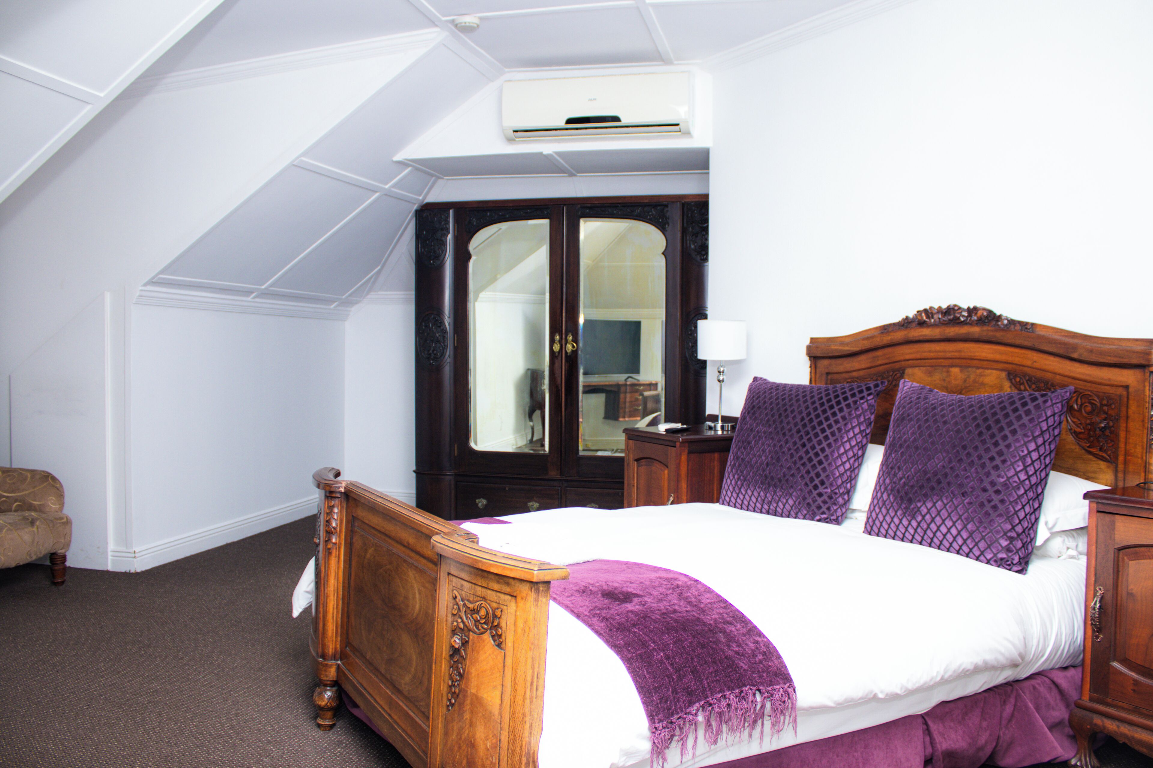 A bedroom with a wooden bed, a dark wooden wardrobe, and a white ceiling with an air conditioning unit.
