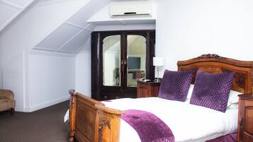 A bedroom with a wooden bed, a dark wooden wardrobe, and a white ceiling with an air conditioning unit.