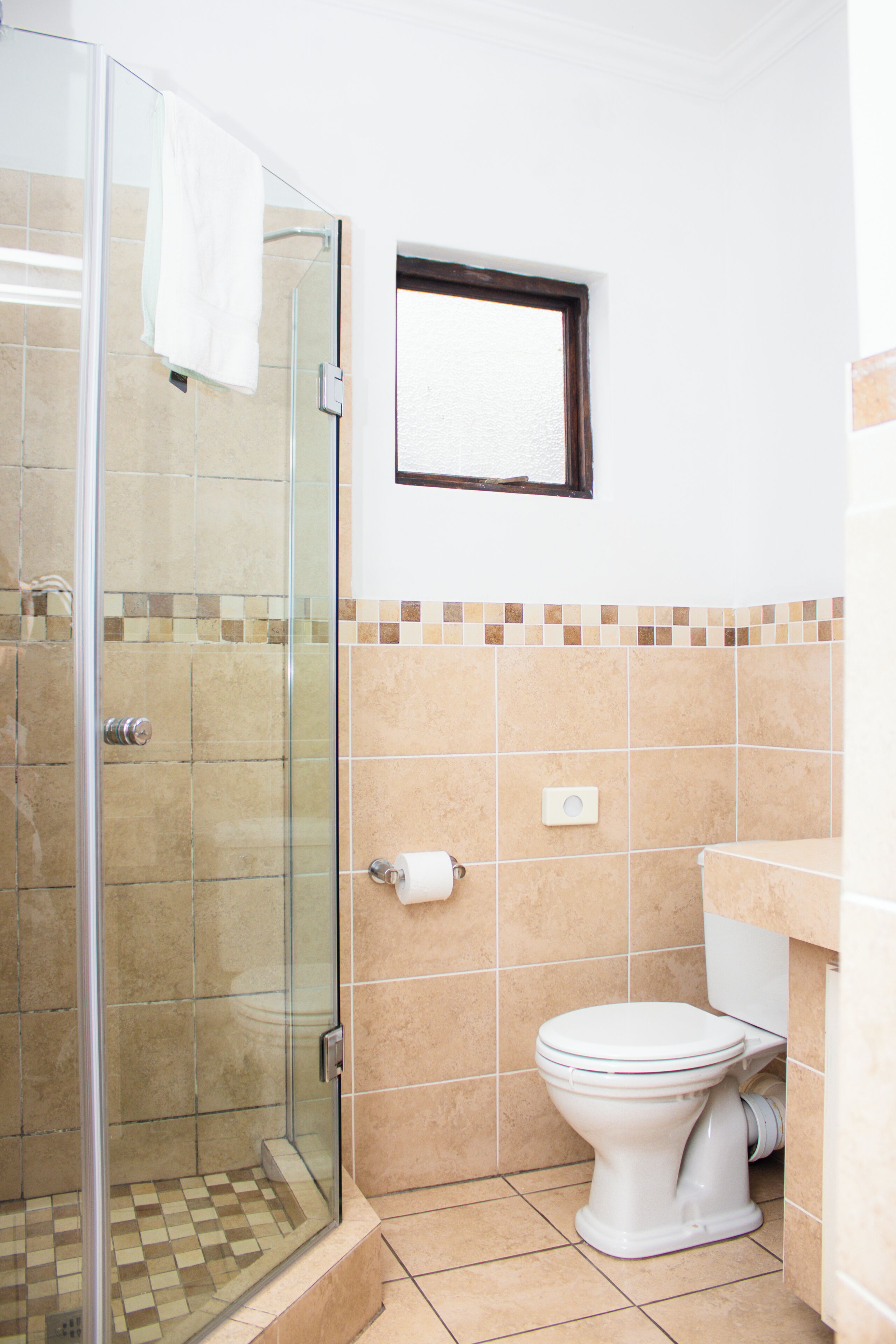 A bathroom with a glass shower enclosure, a toilet, and a small window above the toilet.