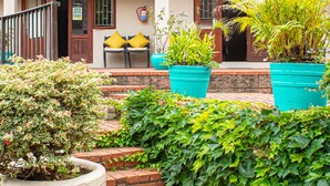 Una casa de dos pisos con entrada de ladrillo, un pequeño porche con cojines amarillos y plantas en macetas.