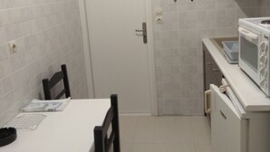 A compact kitchen with white cabinets, a microwave, and a dining table with chairs. - Sea Front Old Town (Rethymno)