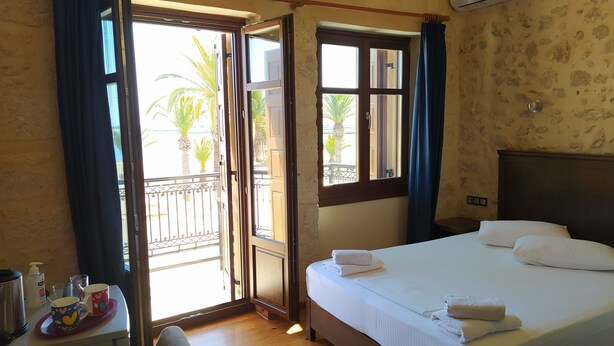 A hotel room with a bed, a desk with a chair, a window with curtains, and an air conditioning unit. - Sea Front Old Town (Rethymno)
