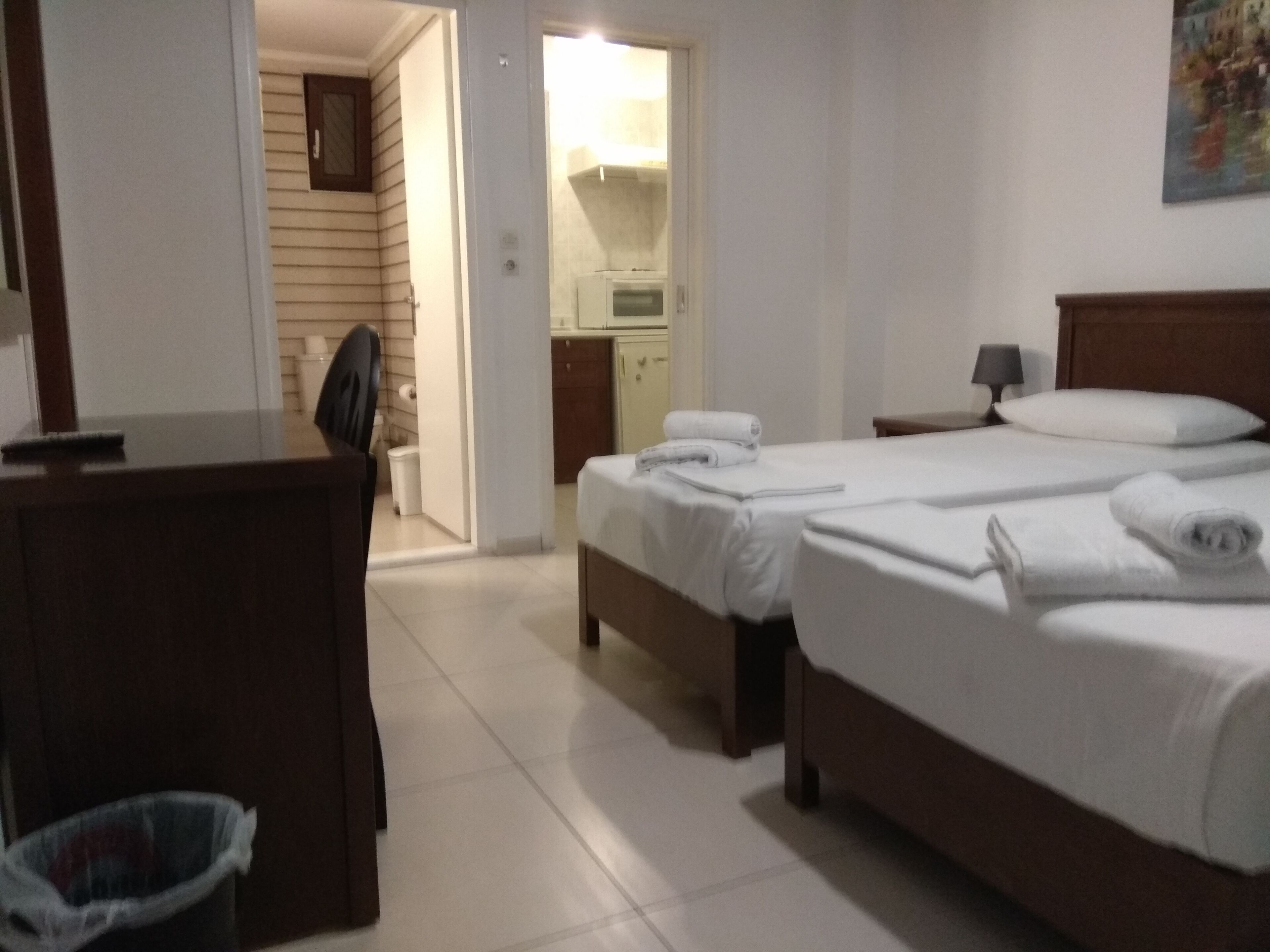 Ett hotellrum med två sängar, ett skrivbord, en stol, en papperskorg och ett badrum som syns genom en öppen dörr.