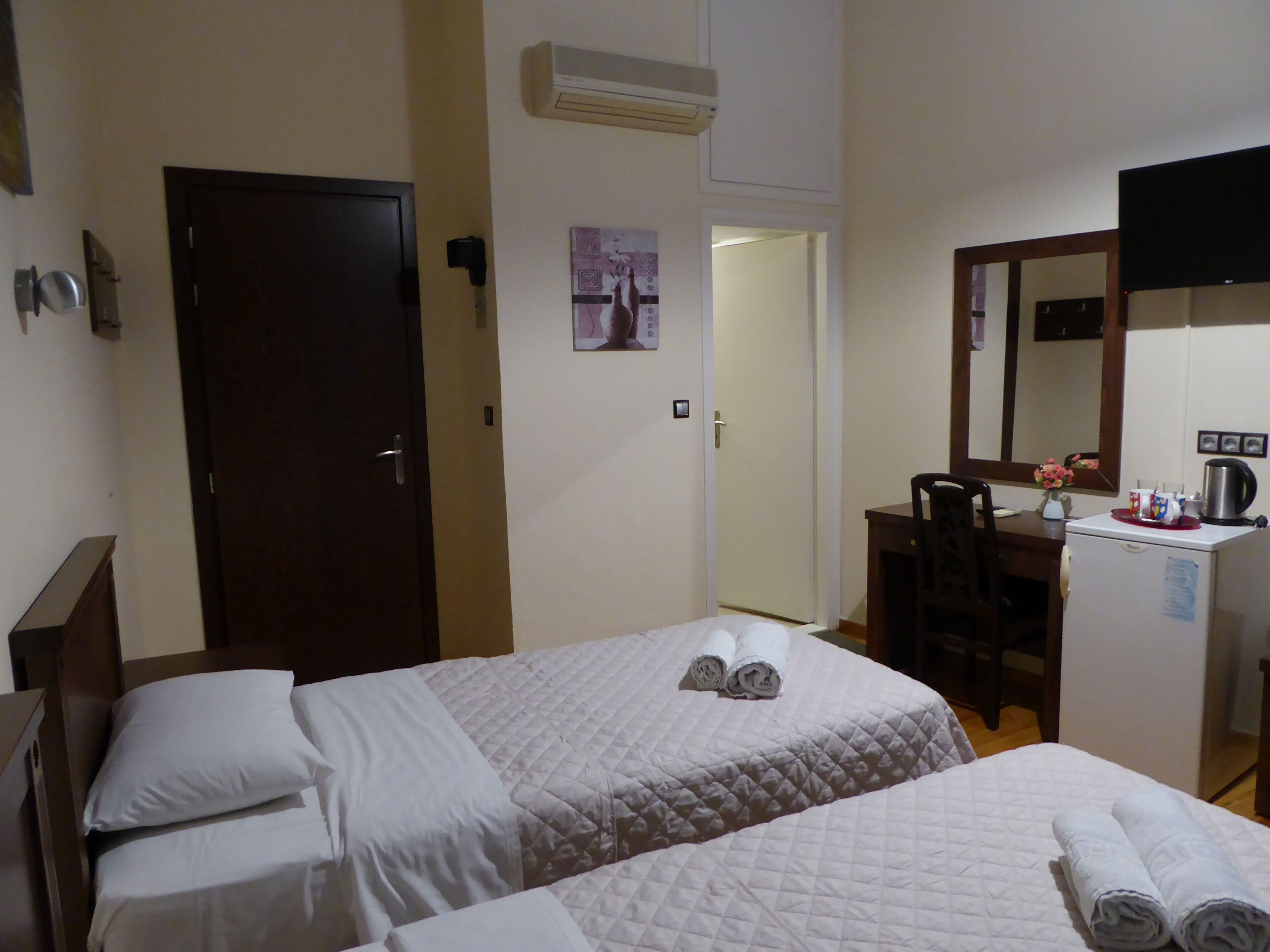 A hotel room with two beds, a desk with a chair, a mirror, and an air conditioning unit.